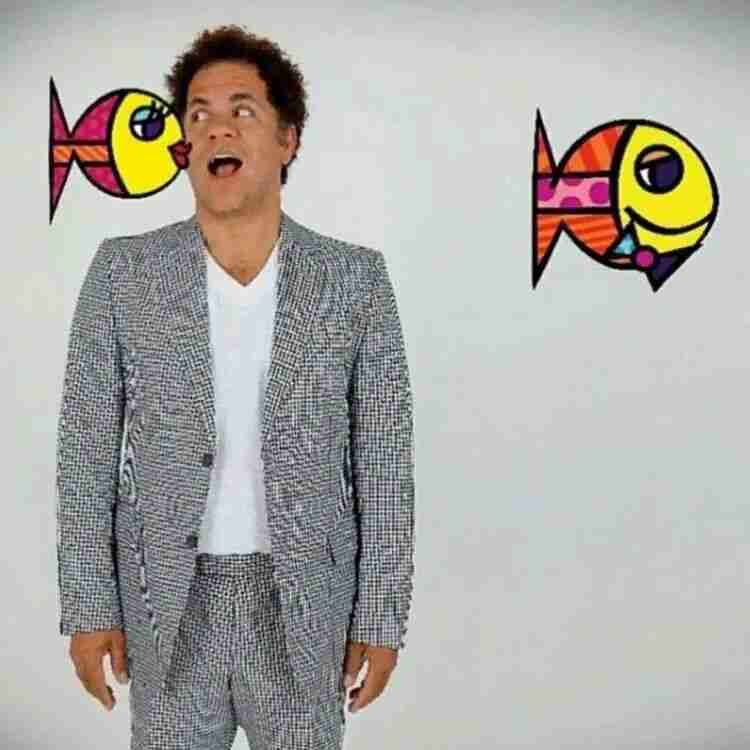 Romero Britto posing playfully between two of his colourful pop-art fish