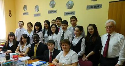 Group photo of students and teachers in a classroom decorated with clocks showing world cities, representing international exchange