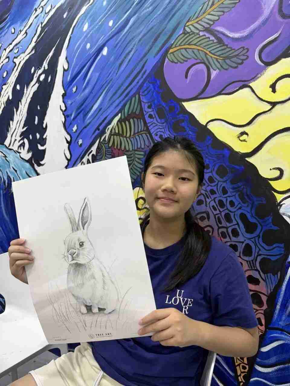 A student presenting her finely shaded rabbit drawing in front of a mural