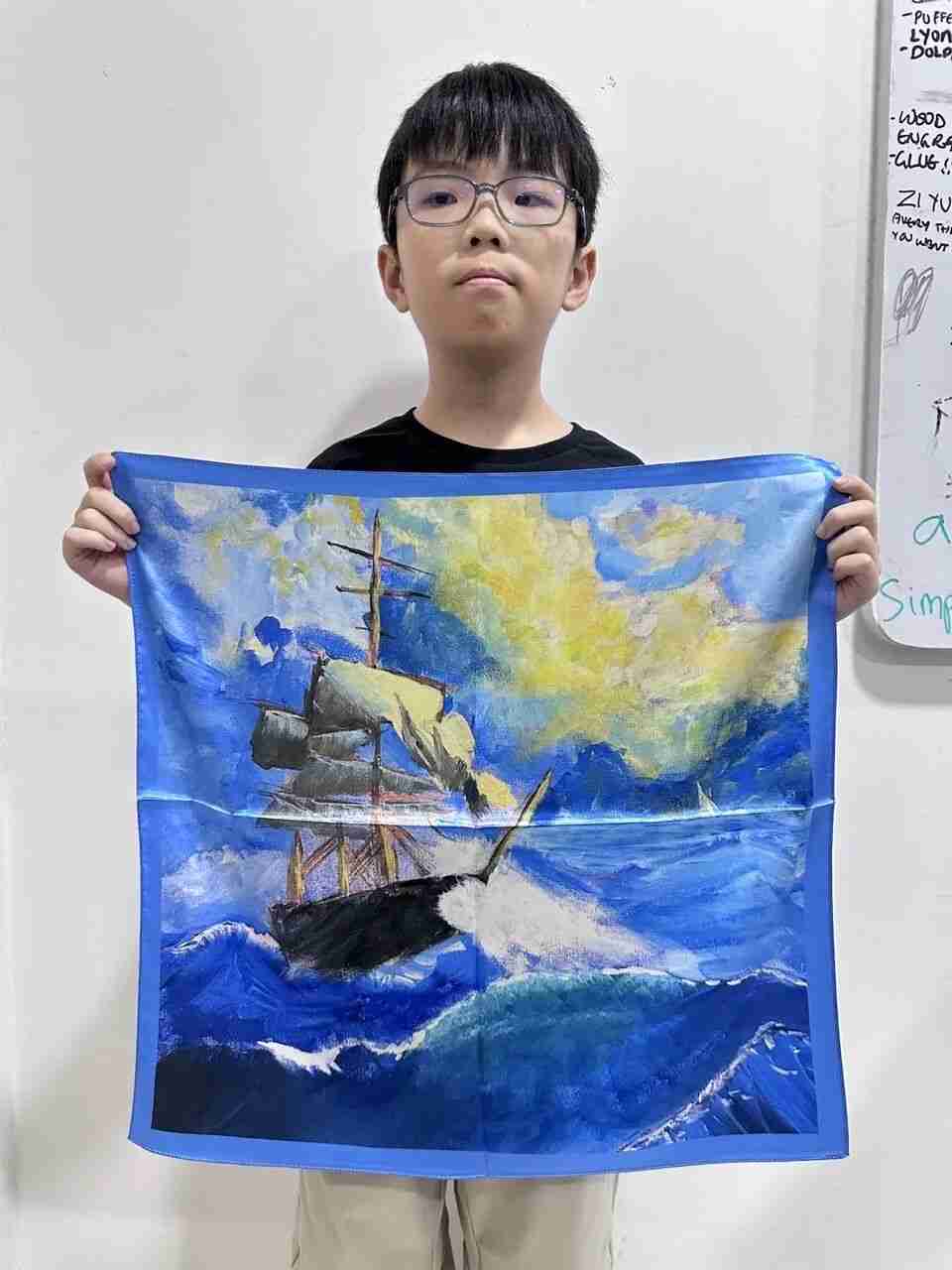 TREE ART student holding up his hand-painted silk scarf featuring a sailing ship on stormy seas
