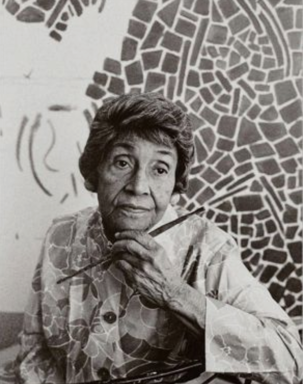 Black-and-white portrait of Alma Thomas seated with a paintbrush, one of her mosaic-style paintings visible behind her