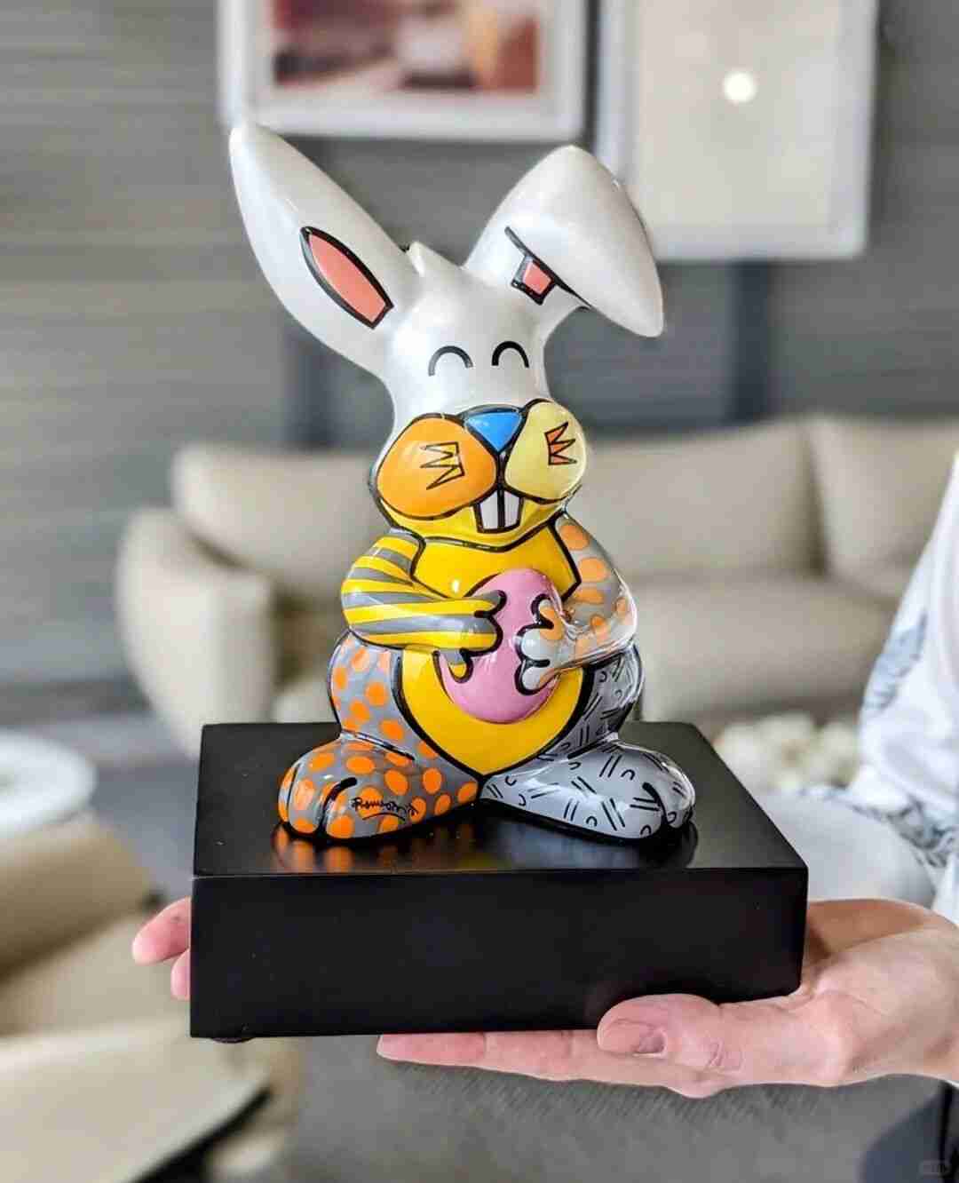 A hand holds Romero Britto's colourful patchwork rabbit sculpture on a black base
