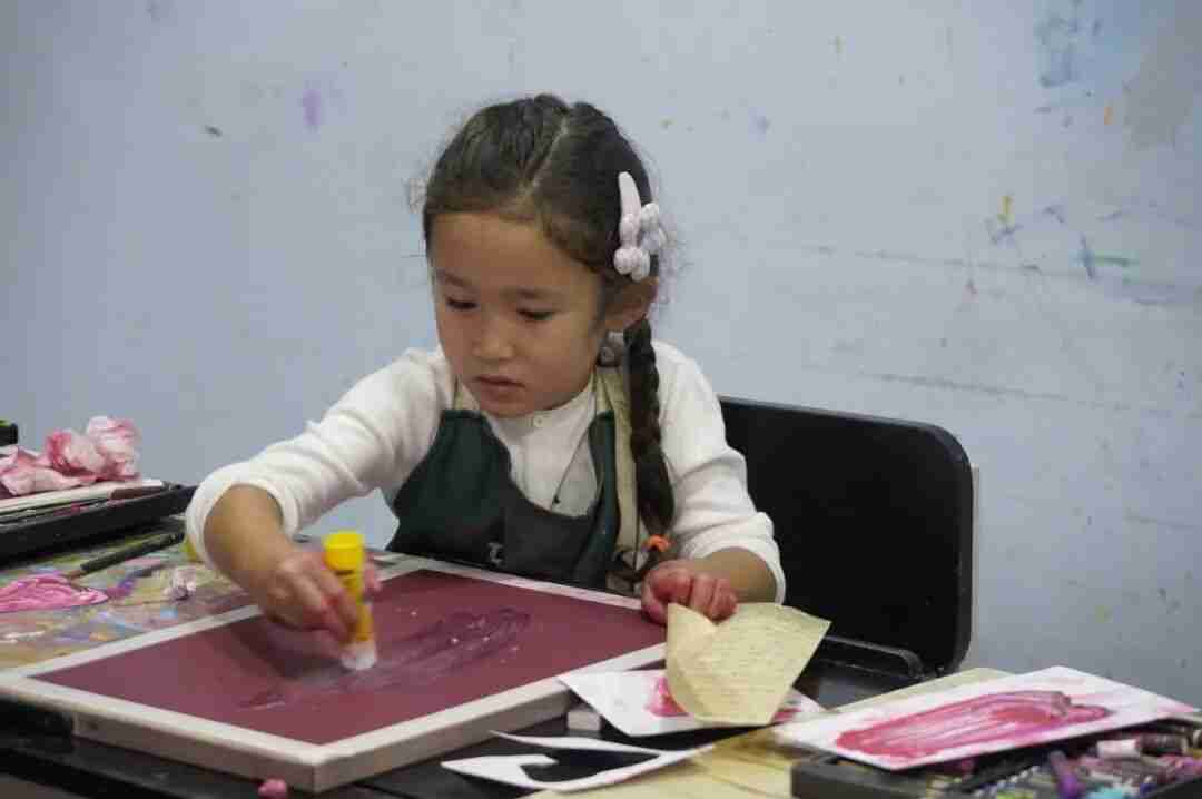 A girl in a TreeArt apron working with glue and paper on a magenta-toned mixed-media piece