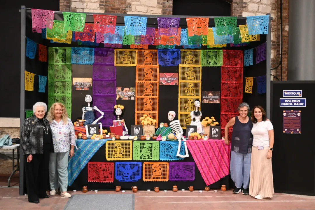 Colorful Day of the Dead-themed exhibition booth with papel picado banners and skeleton figures, with organizers posing for a photo
