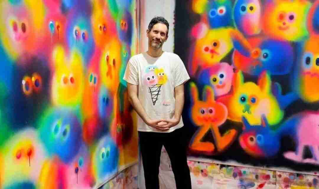 Jon Burgerman standing between two walls covered in his colorful spray-painted character murals