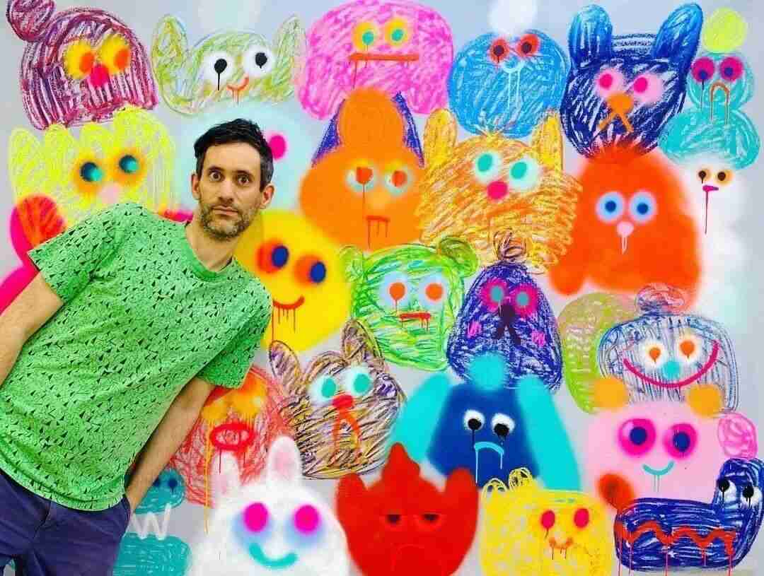 Jon Burgerman standing in front of a wall covered in his colorful doodle monster characters