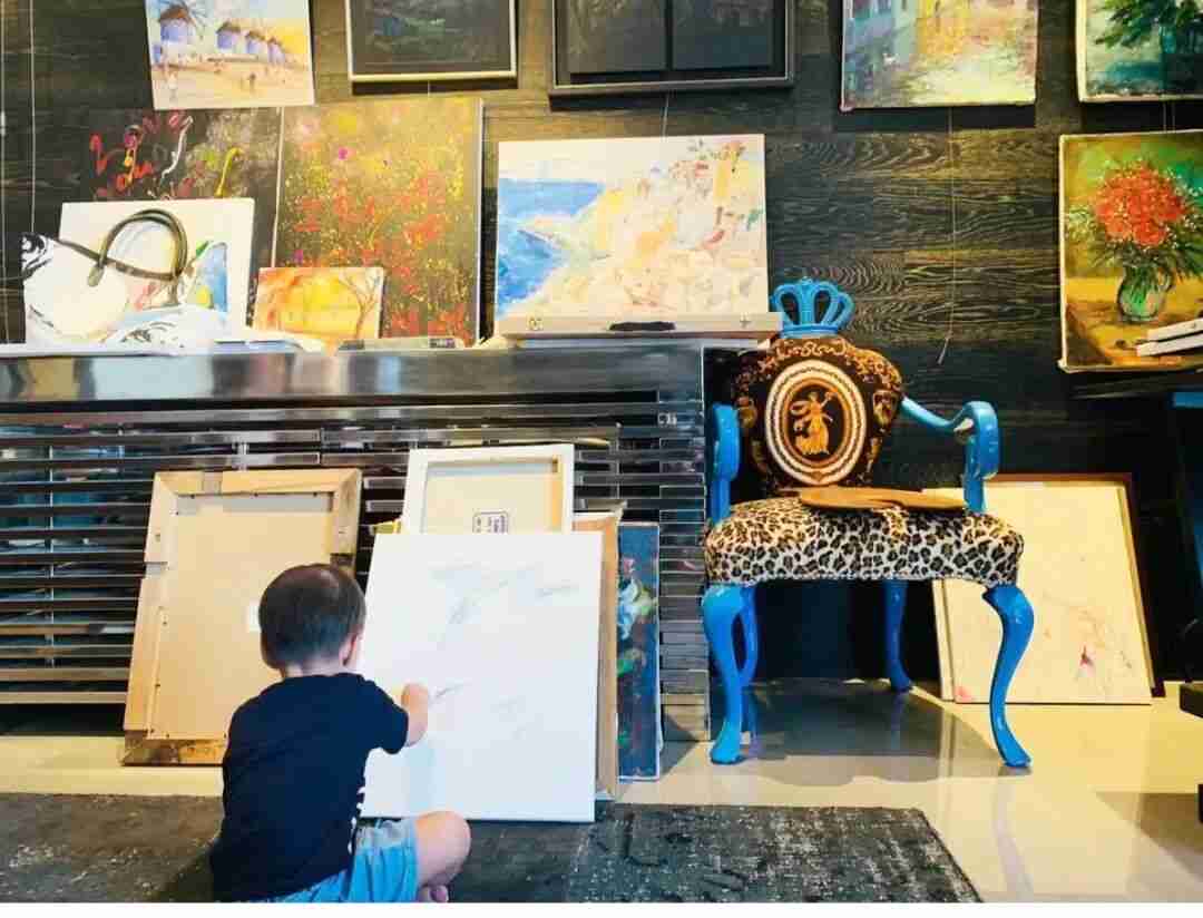 Toddler drawing on a large canvas at home, surrounded by framed paintings