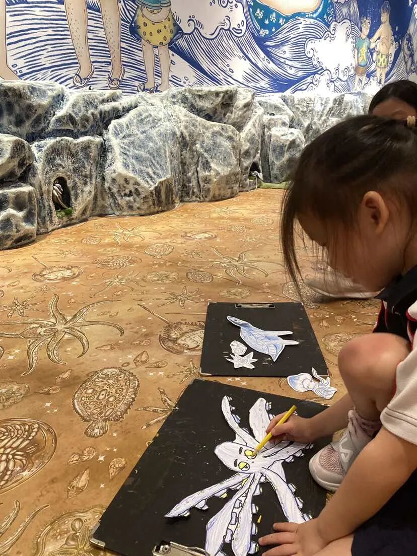 A young girl colours sea-creature cutouts on clipboards in an ocean-themed exhibition space