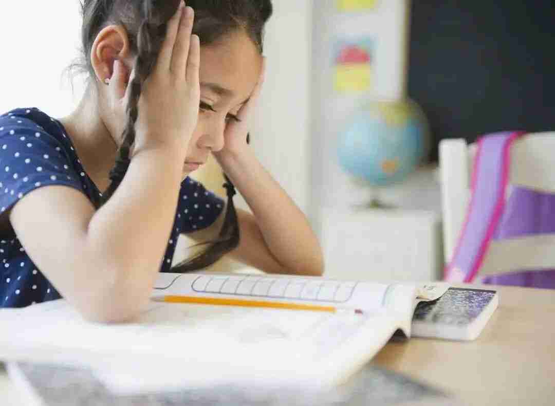 Stressed Primary 6 student resting her head in her hands over an open textbook