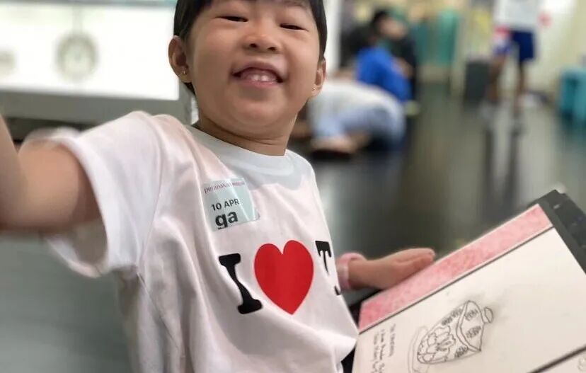 A little girl smiles at the camera while holding her sketchbook