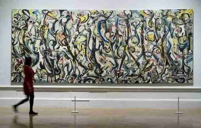 A museum visitor walking past a large drip-style abstract painting