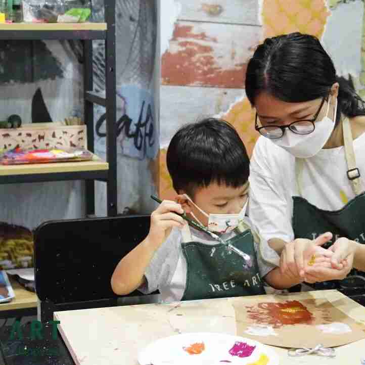 TreeArt teacher guiding a young student's brush during a painting class