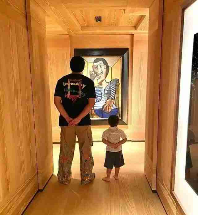 A father and young child standing before a modern portrait painting in a gallery corridor