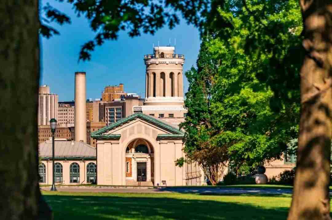 University campus building with a tall domed tower and smokestack, framed by trees