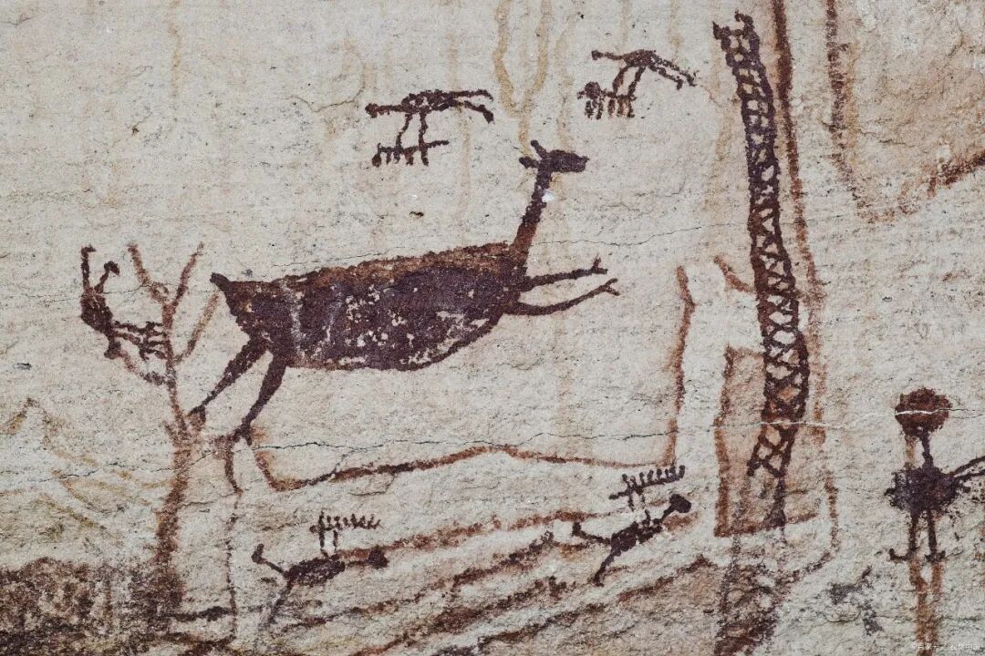 Ochre cave painting of a leaping deer with small hunter figures on a rock wall