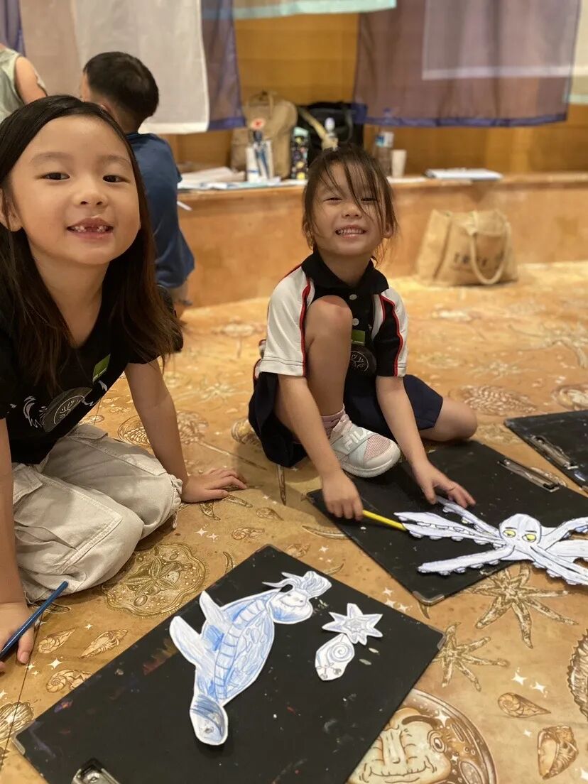 Two smiling TreeArt students drawing sea creatures on black paper