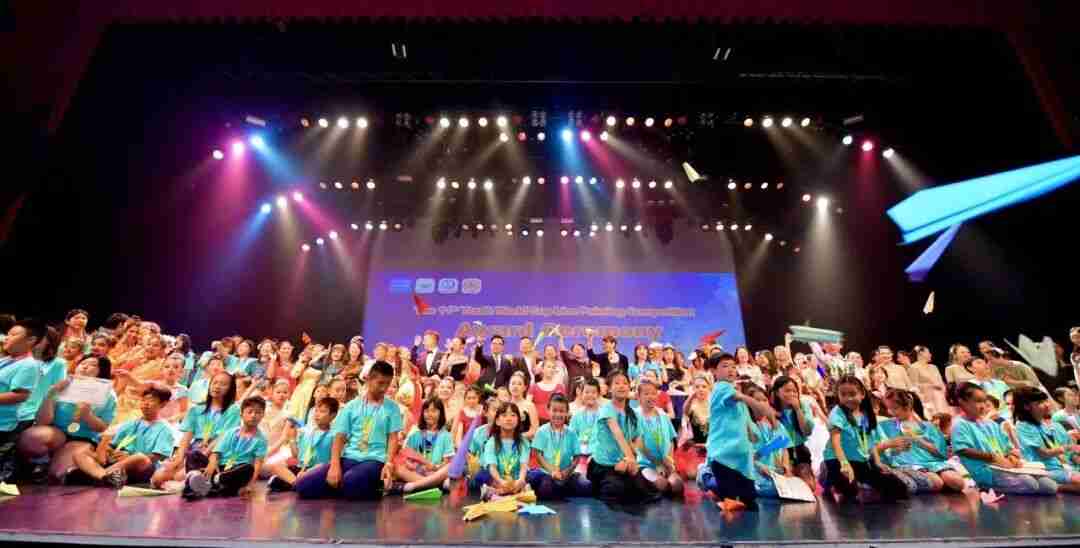 Children celebrating on stage with paper airplanes at the Youth World Cup Painting Competition award ceremony