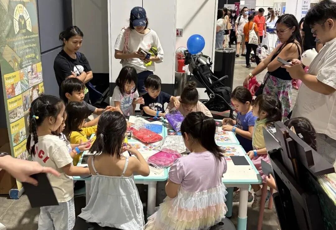 Children gathered around a table creating art together at a TreeArt exhibition booth, with parents looking on
