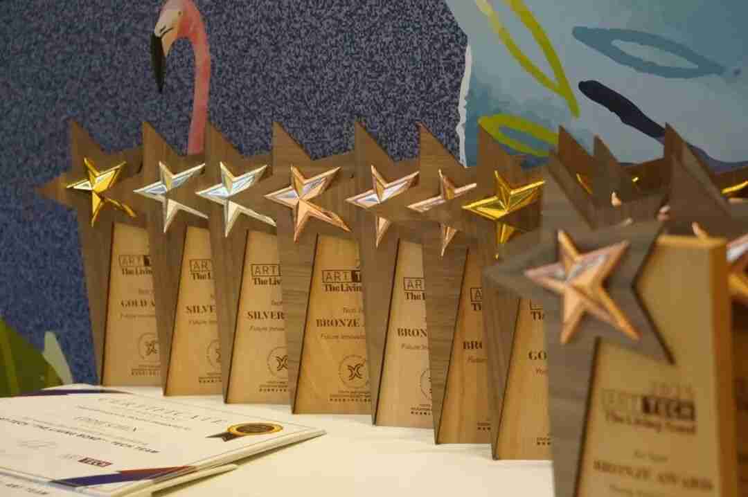 Row of gold, silver, and bronze star-shaped ART TECH trophies with certificates from a previous year's competition