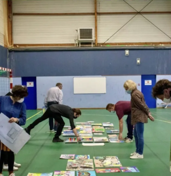 Jury members reviewing children's artwork entries laid out on the gymnasium floor during judging