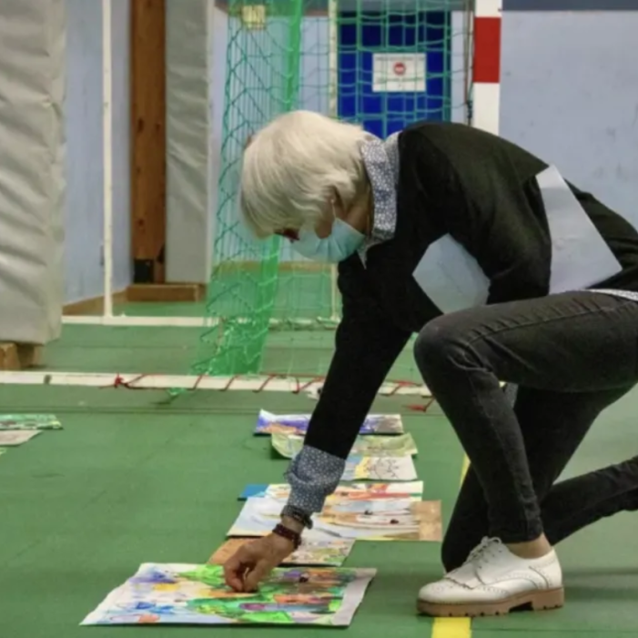 A juror kneeling to closely examine a young artist's painting during the judging process