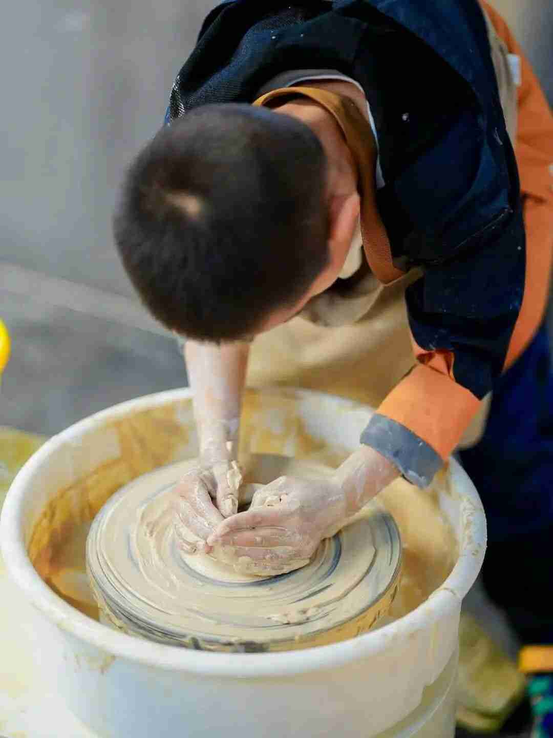 Child shaping clay into a cup on a pottery wheel
