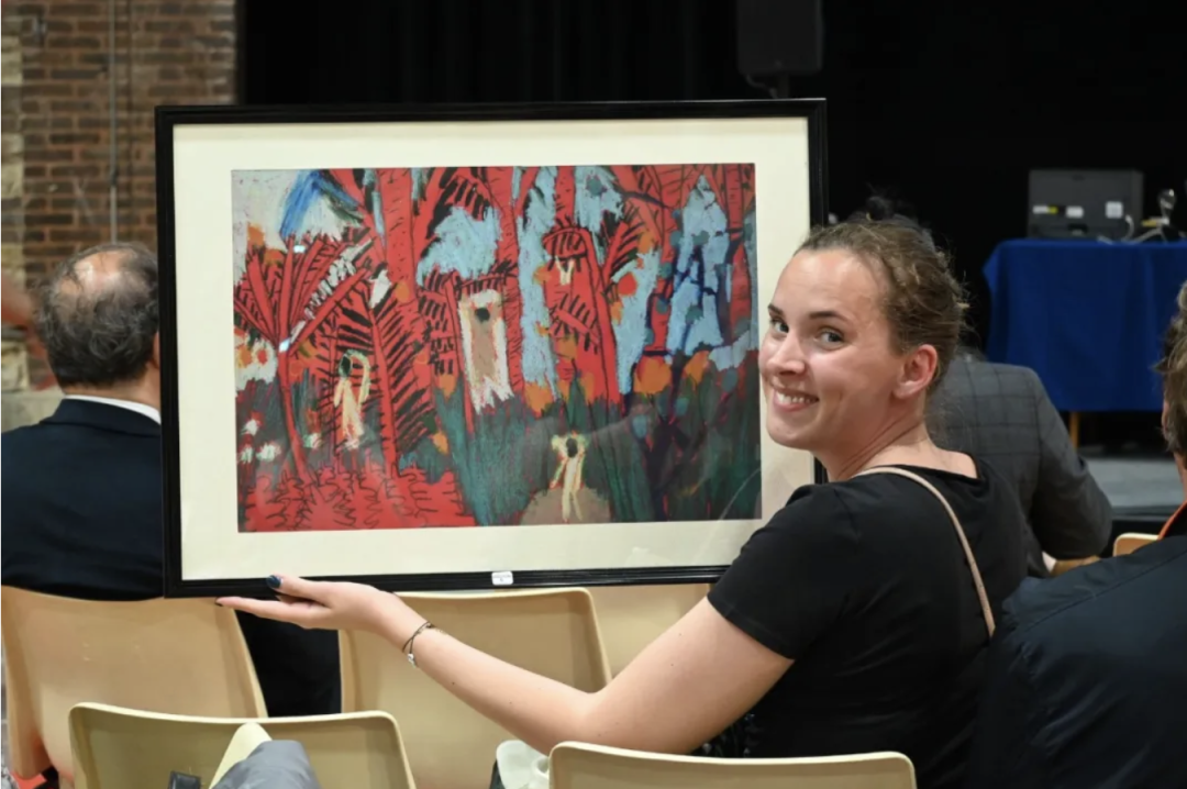 A young award winner smiling while holding her framed winning artwork at the ceremony