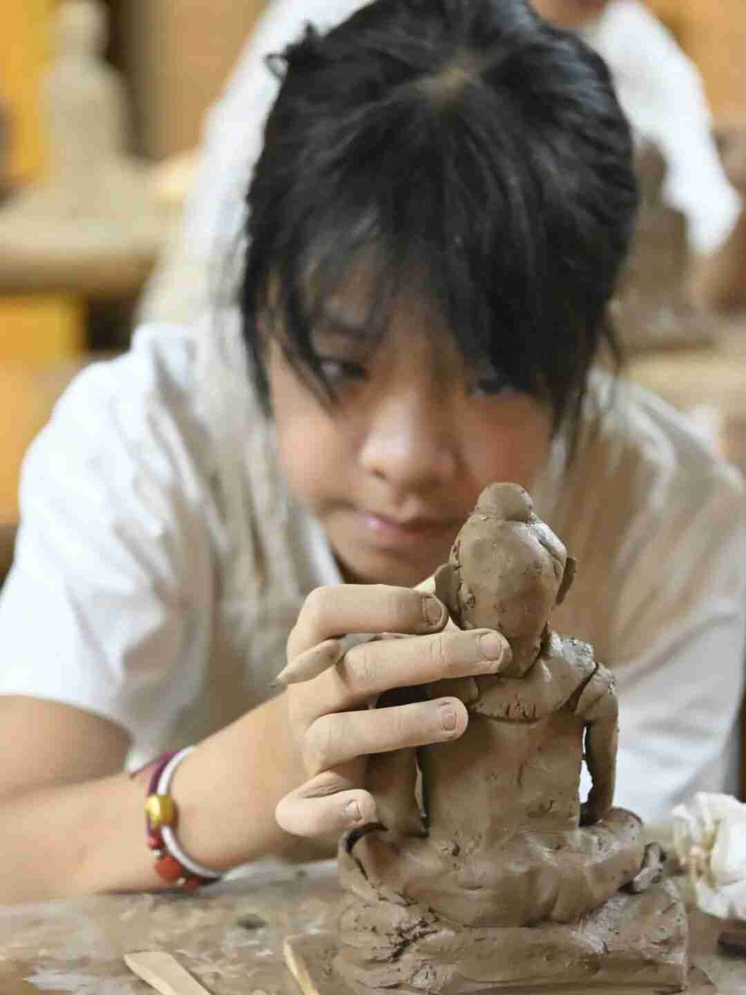 A child carving fine details into a clay sculpture