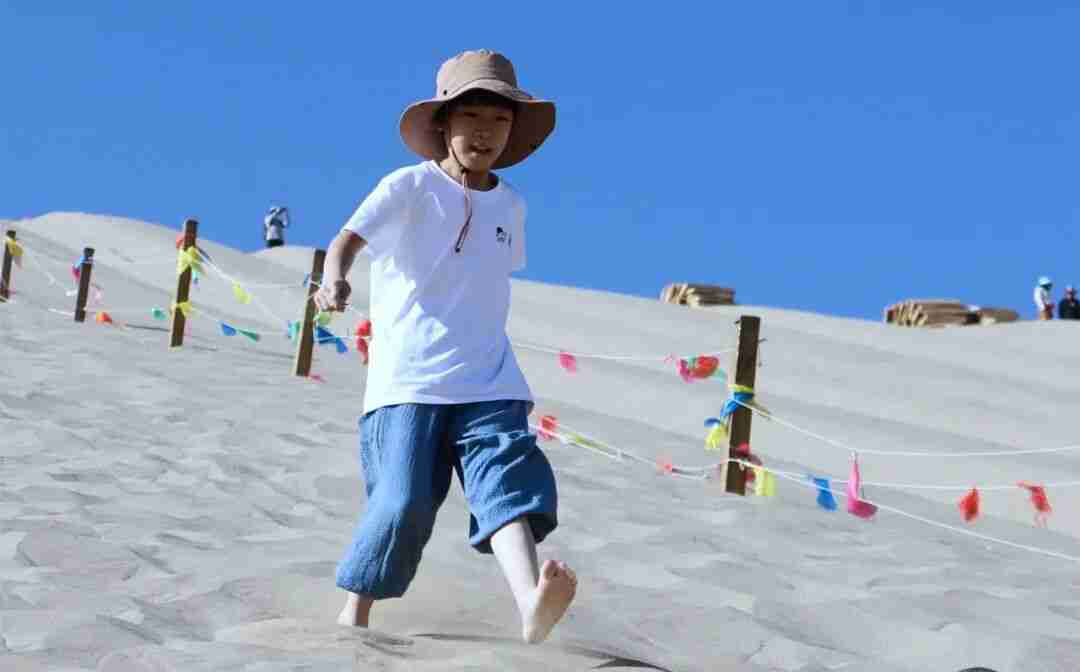Children climbing the golden dunes of Mingsha Mountain