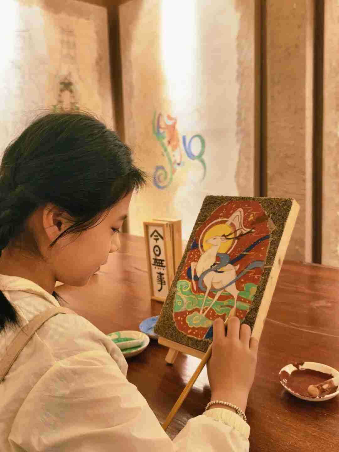 A child tracing mural lines onto a clay tablet