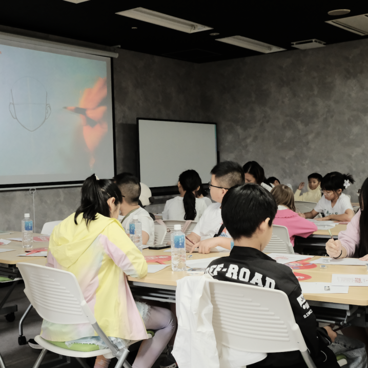 Children in a classroom studying a manga face-drawing demonstration projected on screen at AMPS Anime School