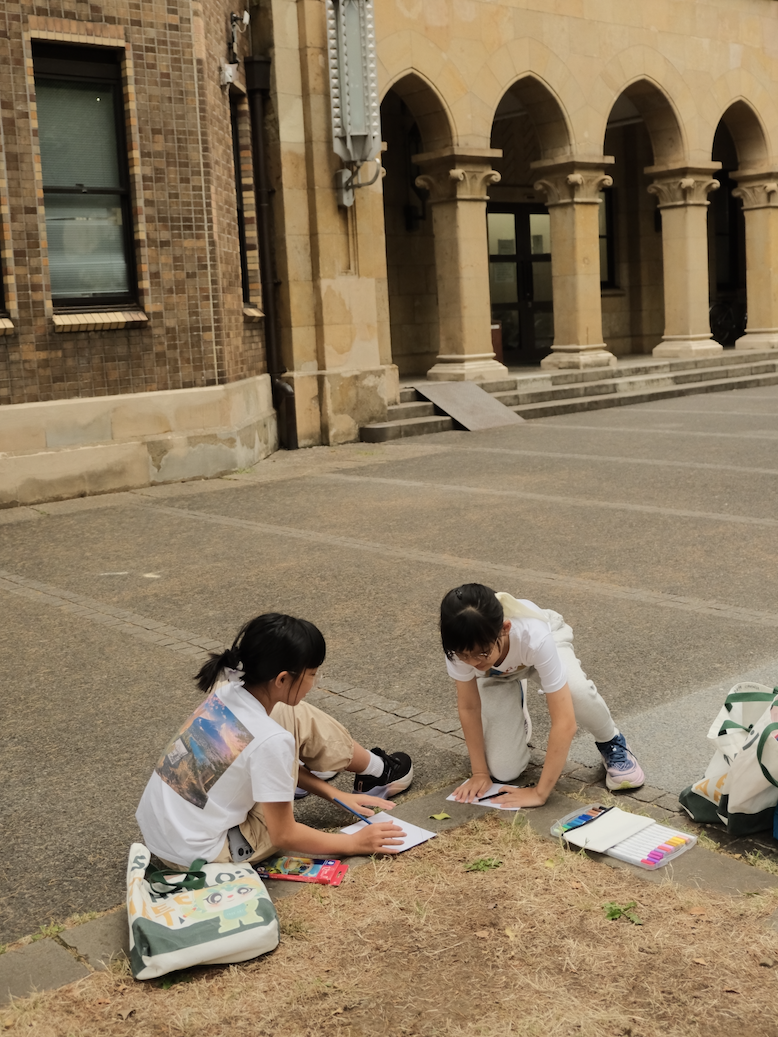 Two children sketching the historic red-brick architecture of the University of Tokyo
